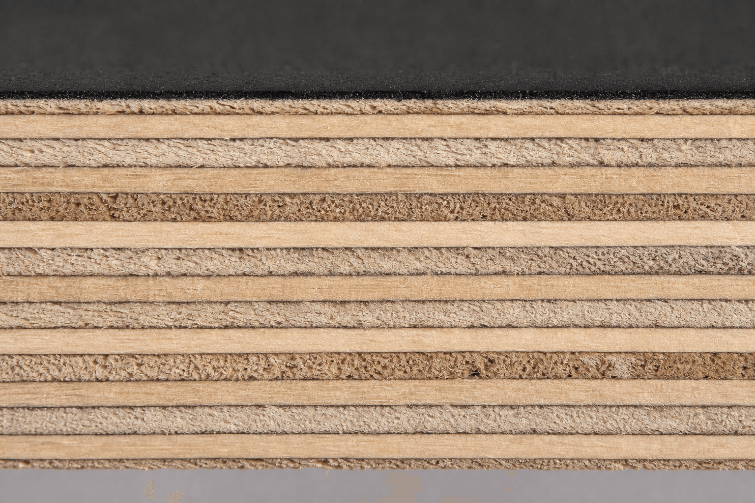Macro of a film-faced plywood edge: alternating smooth and end-grain veneer plies under a paper-thin black phenolic film